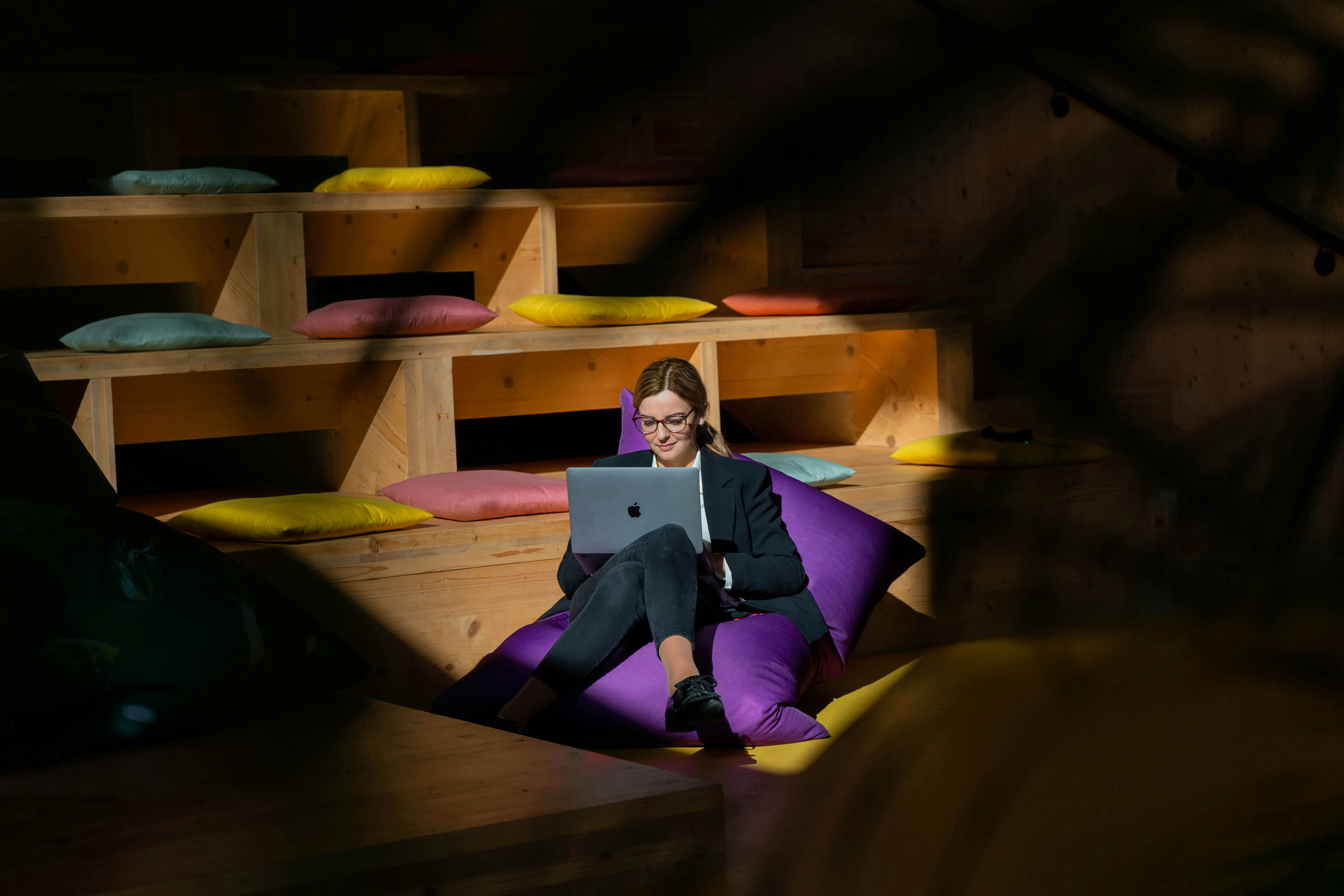 a woman sitting on a bean bag chair using a laptop, Woman remote work bean bag coworking office