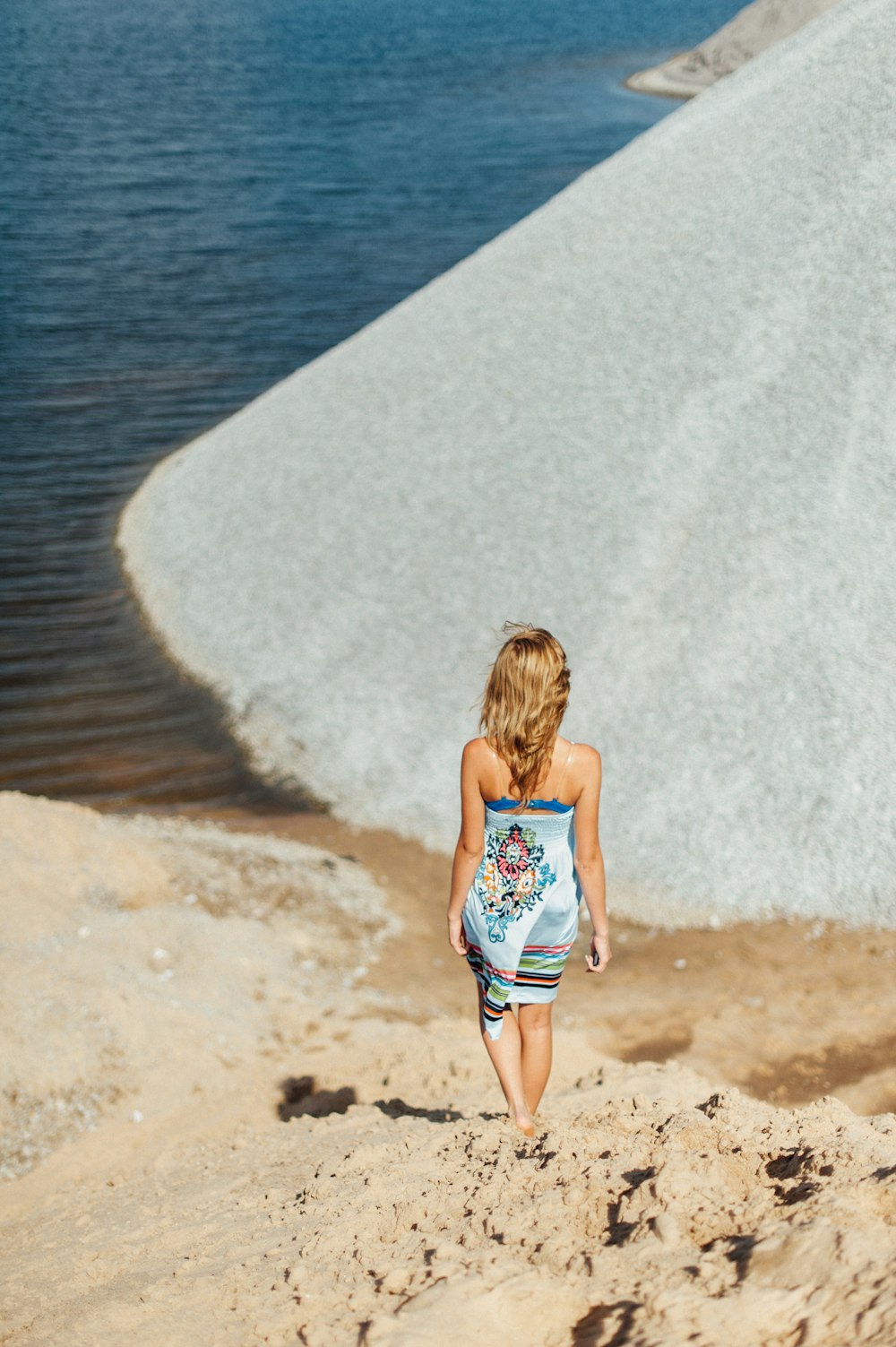 a little girl walking on a beach next to a body of water