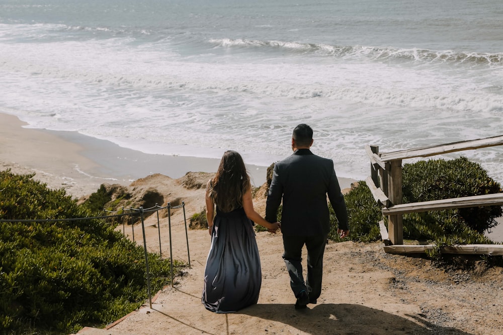 a man and a woman walking up a set of stairs towards the ocean