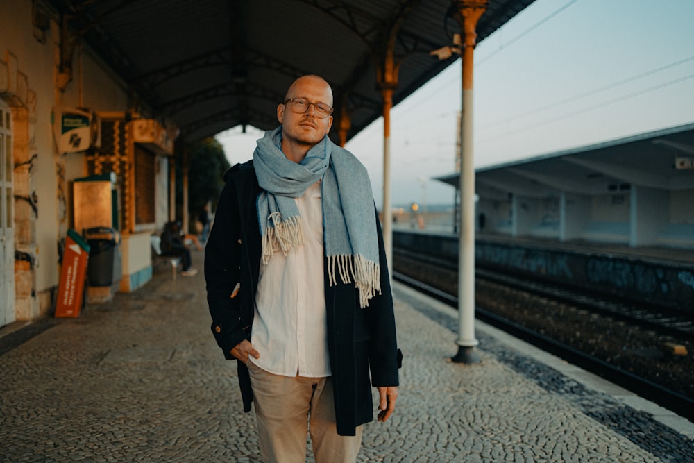 a man wearing a scarf standing in front of a train station