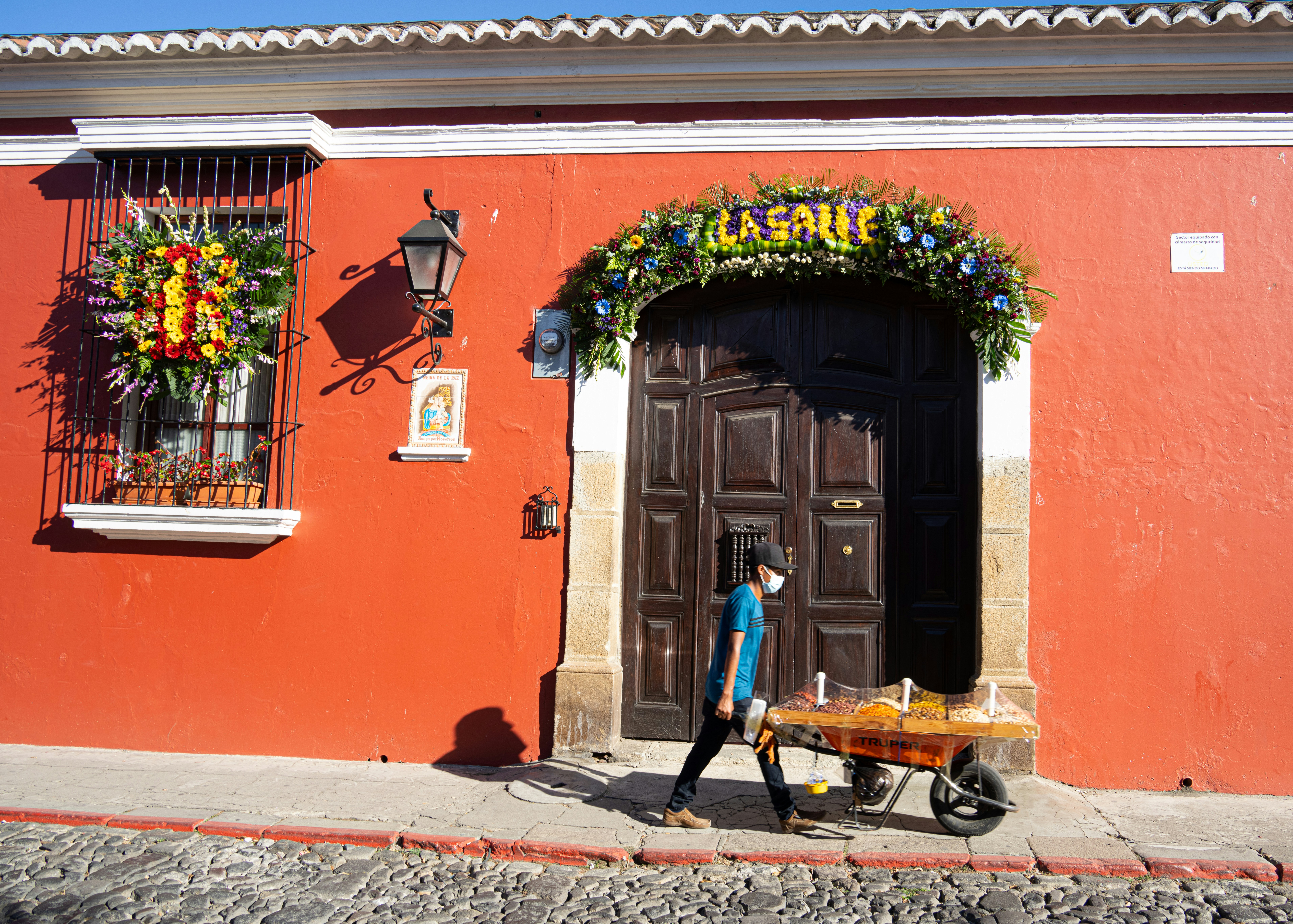 a woman walking past a red building with a cart of flowers
