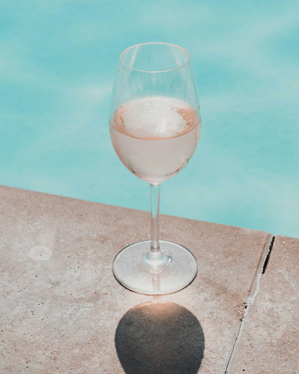 a glass of wine sitting next to a swimming pool