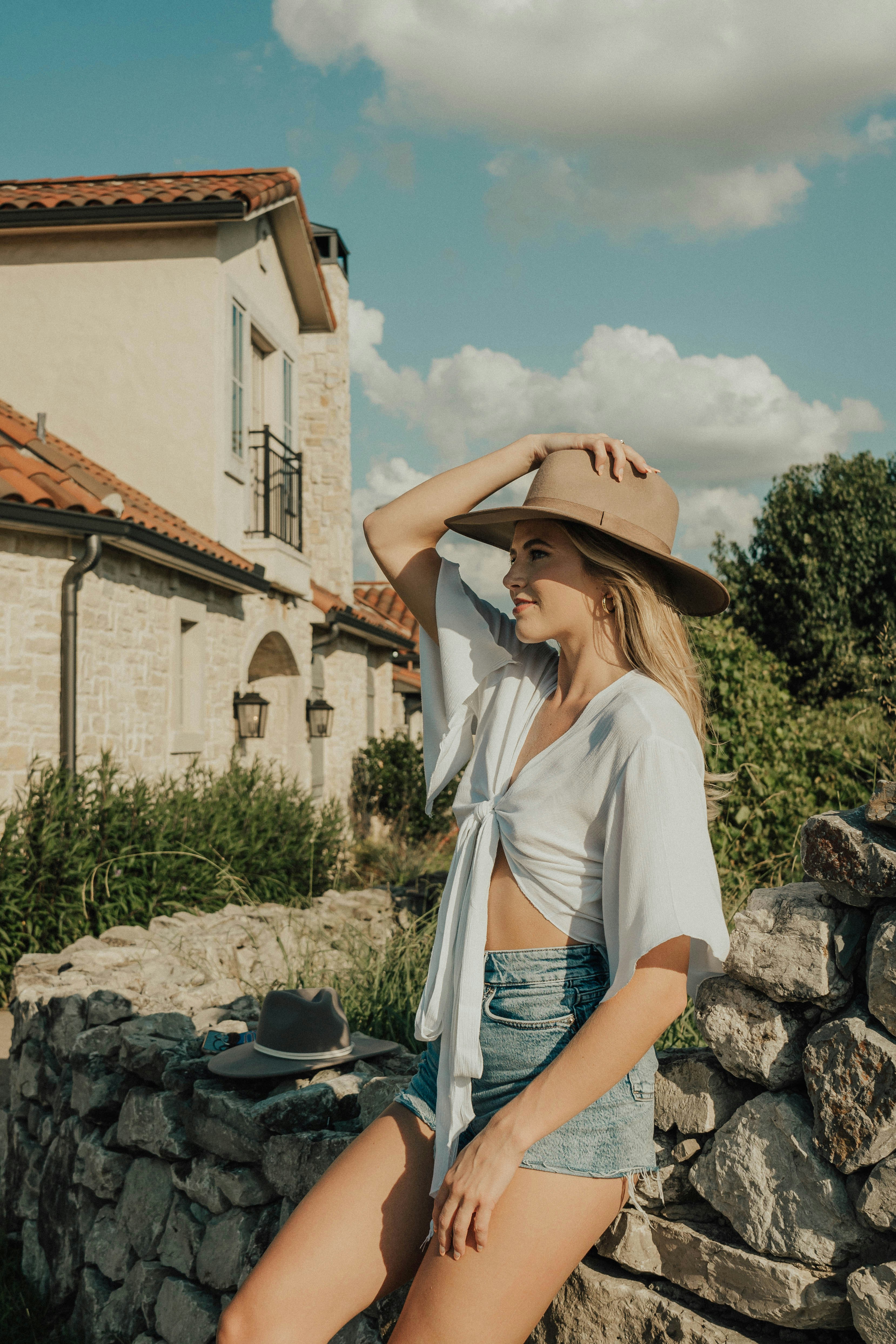 a woman in a hat is sitting on a stone wall