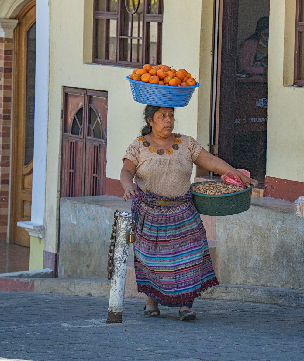 a woman carrying a basket of oranges on her head