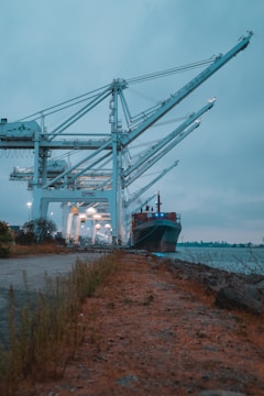 A heavy-lift crane loading oversized industrial equipment onto a cargo ship at dusk