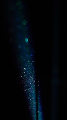 A dark background with scattered bokeh-like lights in various colors, predominantly blue and green, creating an ethereal or abstract effect.