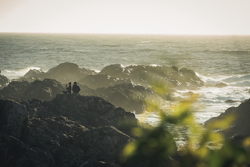 a couple of people sitting on top of a rock near the ocean