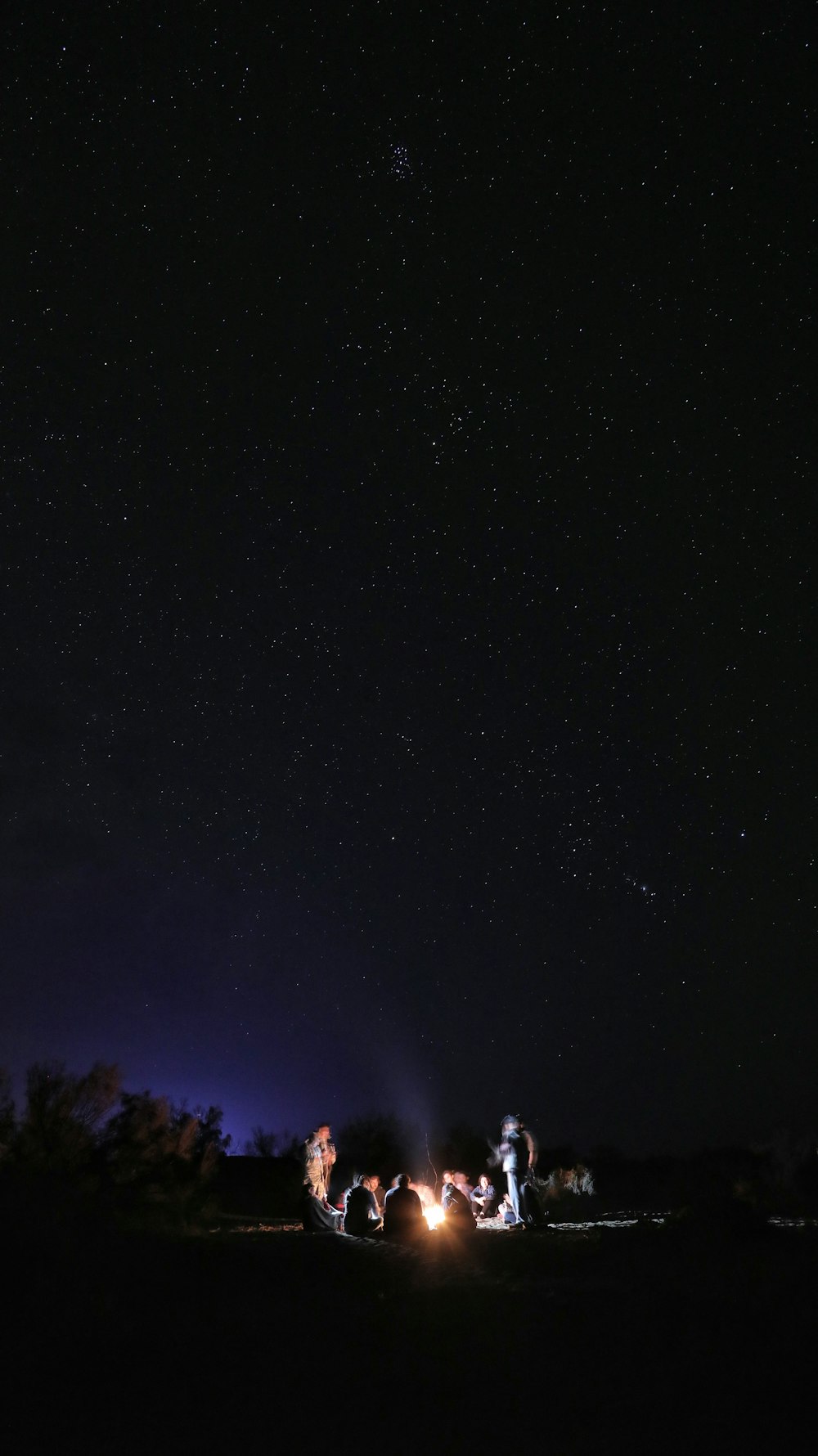 a group of people sitting around a campfire at night