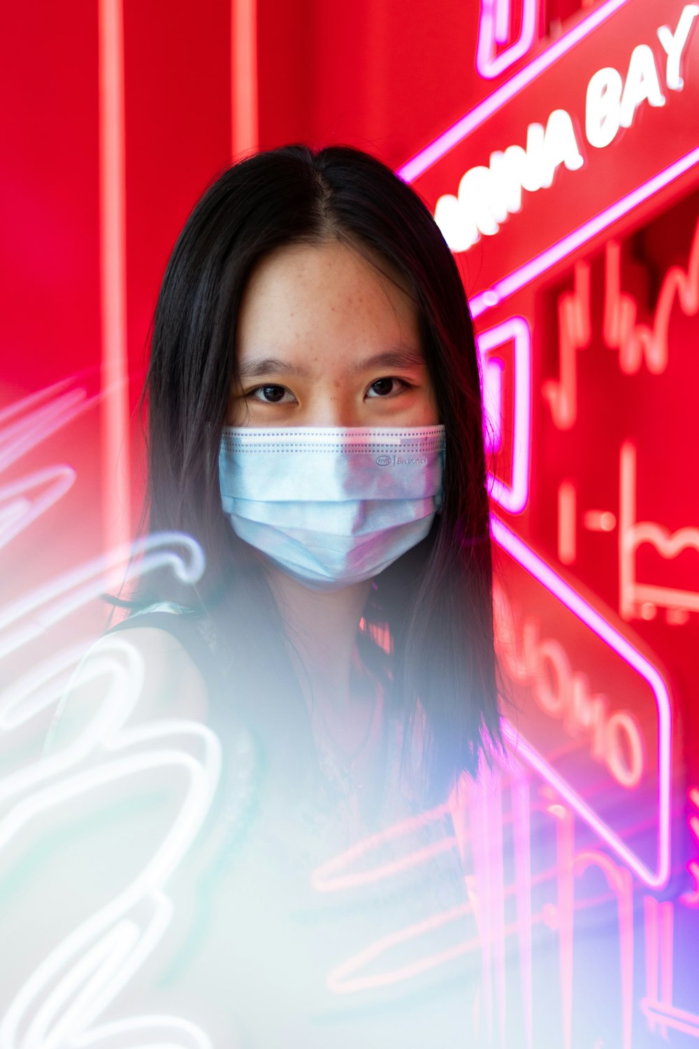 a woman wearing a face mask in front of neon signs