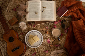 A small, bright red music box next to a cozy book and a cup of tea on a bedside table