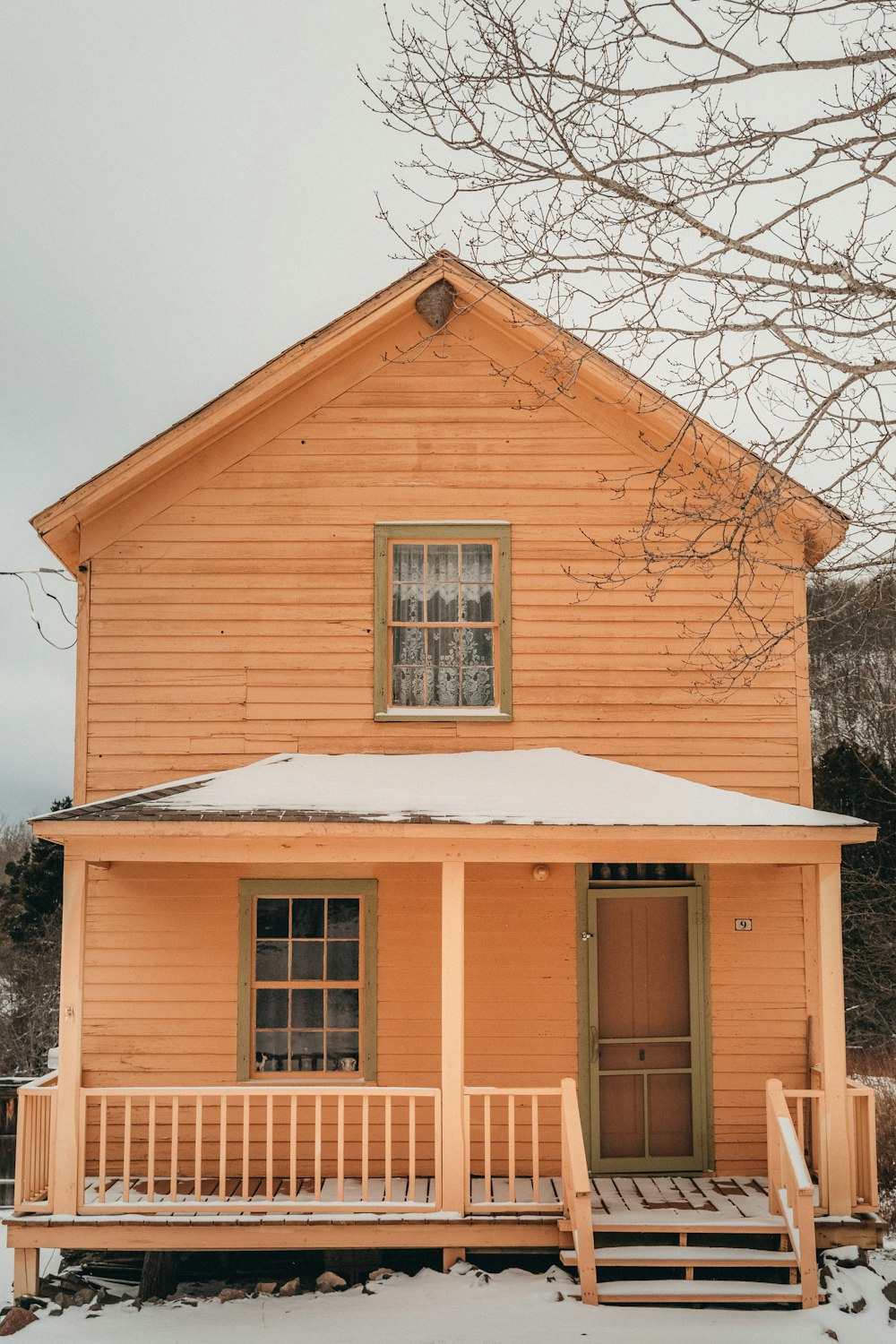 a yellow house with a porch and snow on the ground