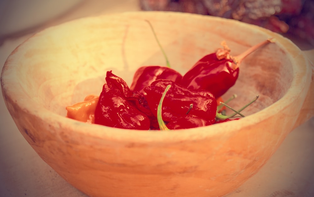 a wooden bowl filled with red peppers on top of a table