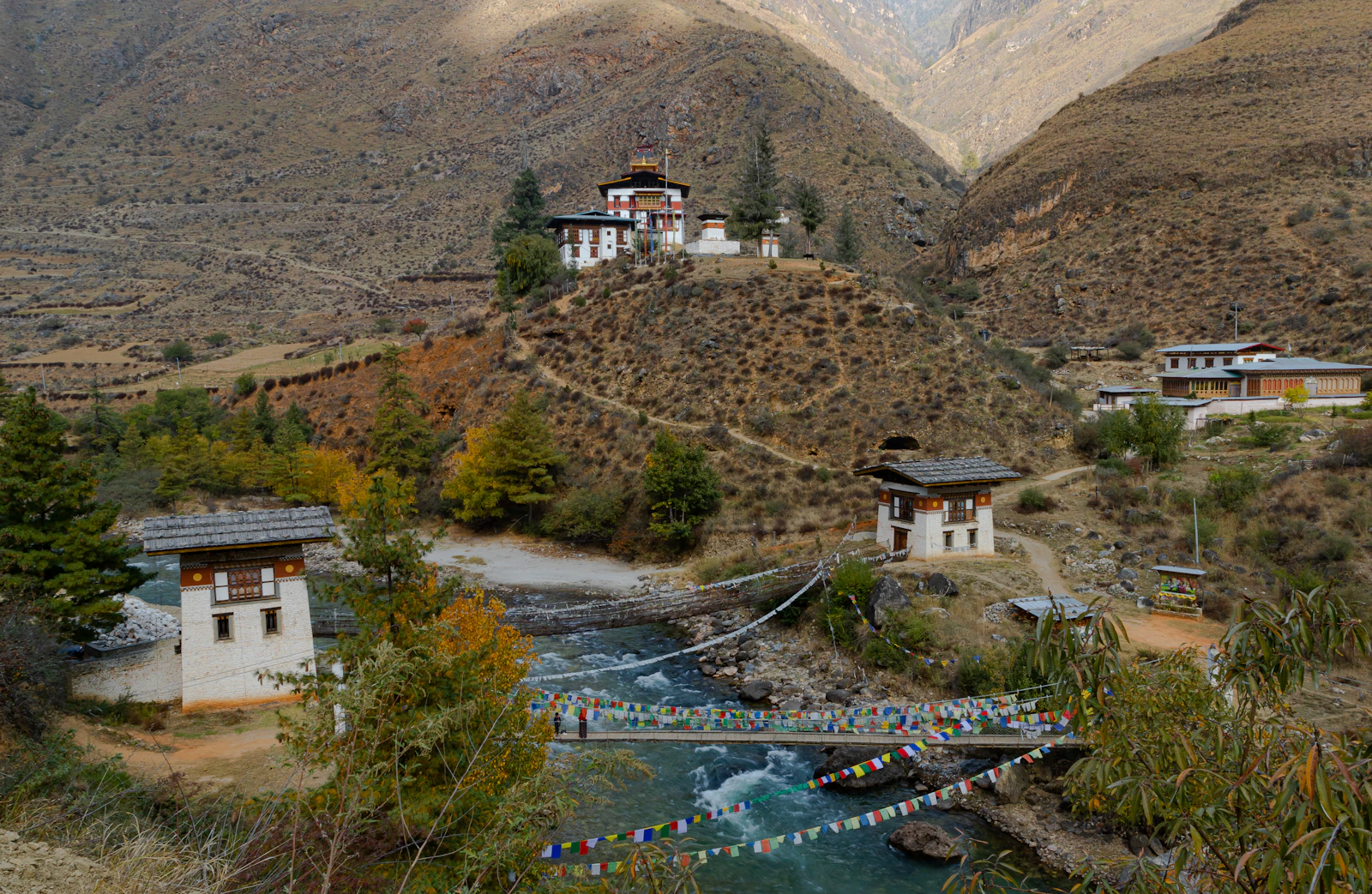 Iron chain bridge hung with prayer flags over the Paro Chhu below Tamchog Lhakhang, the temple on its dry hillside above