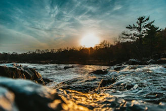 the sun is setting over a river with rocks