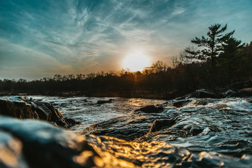 the sun is setting over a river with rocks