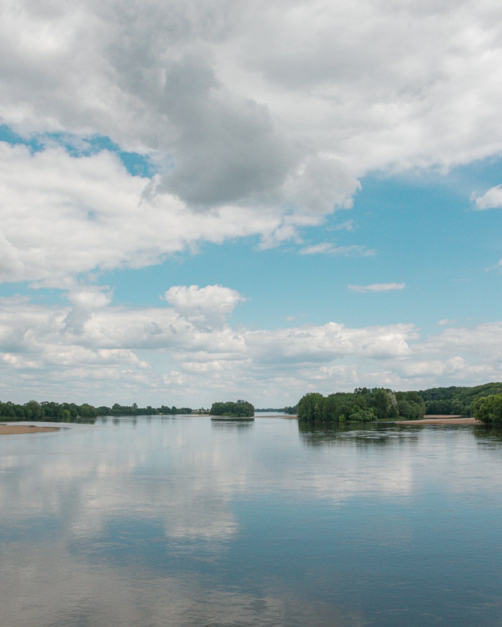 a body of water surrounded by trees and clouds