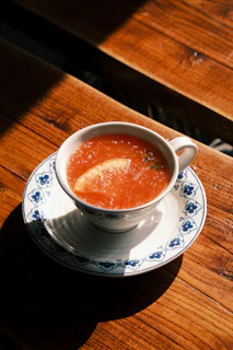 a bowl of soup on a saucer on a wooden table