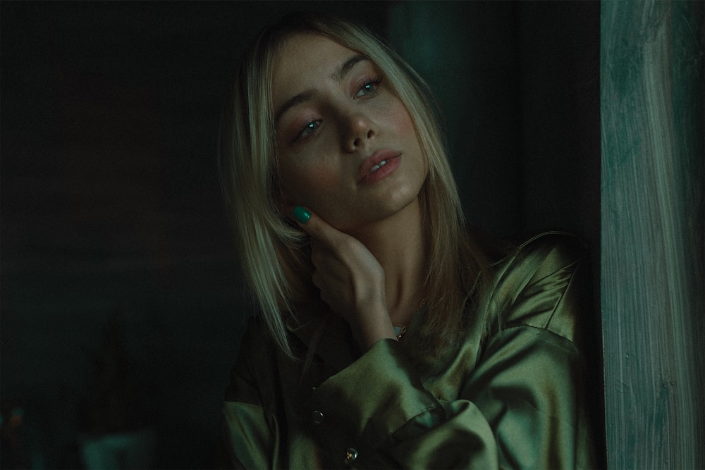 a woman in a green coat leaning against a wall