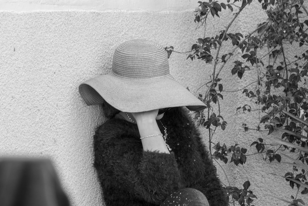 a woman wearing a hat leaning against a wall