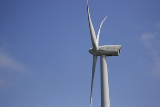 A large wind turbine stands against a clear blue sky, showcasing its long, sleek blades. The structure is modern and designed for harnessing wind energy.