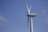 A large wind turbine stands against a clear blue sky, showcasing its long, sleek blades. The structure is modern and designed for harnessing wind energy.