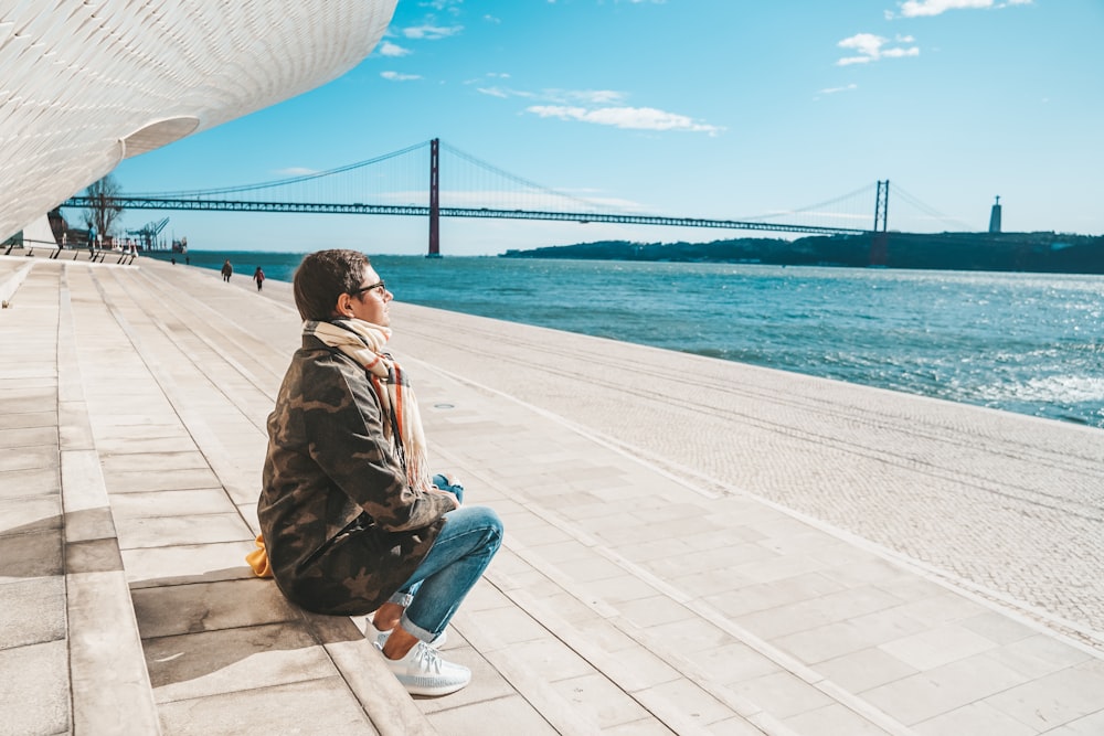 a man sitting on a ledge looking at the water