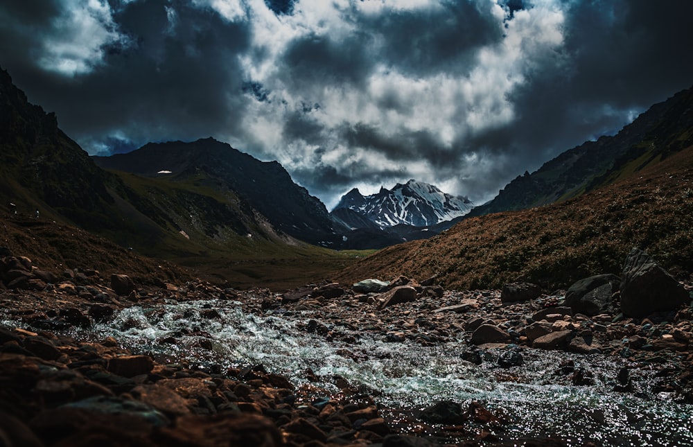 a river running through a rocky valley under a cloudy sky