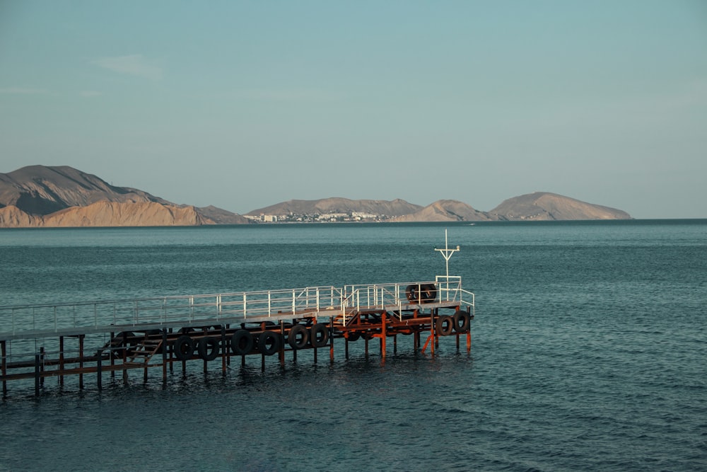 a pier in the middle of the ocean with mountains in the background