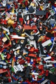 A chaotic and colorful assortment of interlocking plastic building toy bricks, shown in a variety of sizes and shapes, scattered randomly. The pieces are predominantly made up of bright reds, blues, yellows, whites, and blacks.