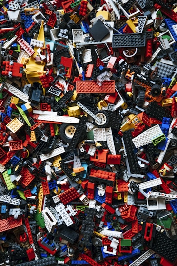A chaotic and colorful assortment of interlocking plastic building toy bricks, shown in a variety of sizes and shapes, scattered randomly. The pieces are predominantly made up of bright reds, blues, yellows, whites, and blacks.