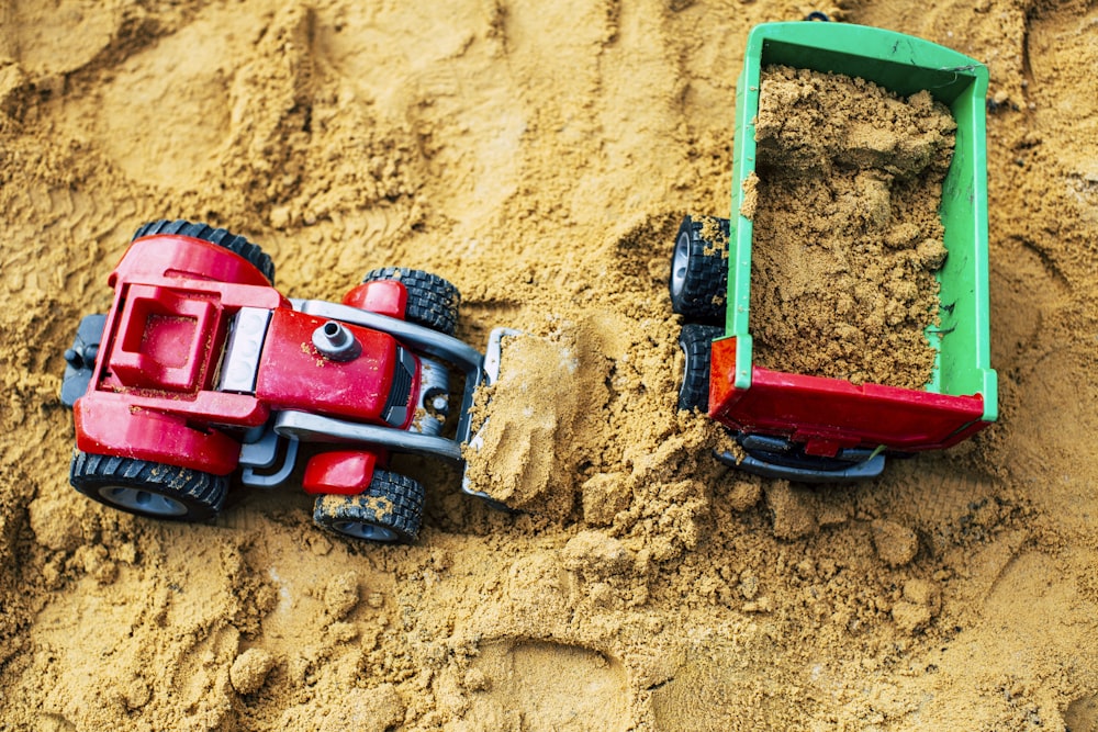 a red toy truck and a green toy car are in the sand
