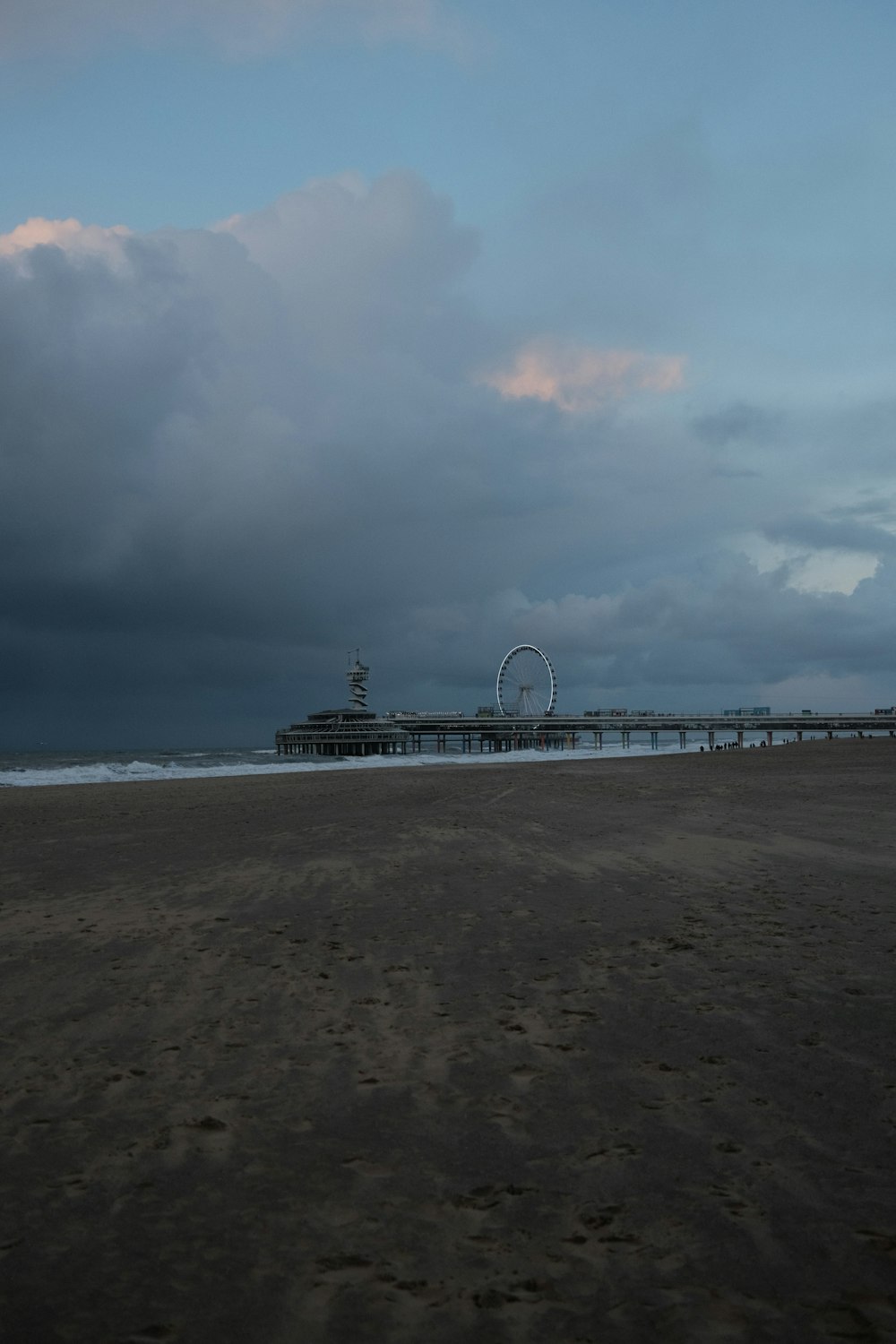 a cloudy day at the beach with a pier in the distance