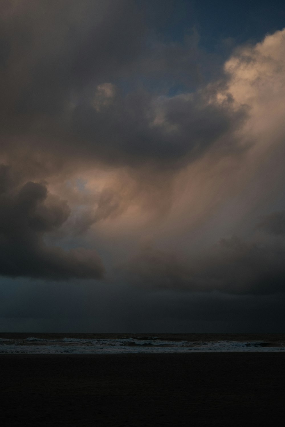 a person on a beach with a surfboard under a cloudy sky