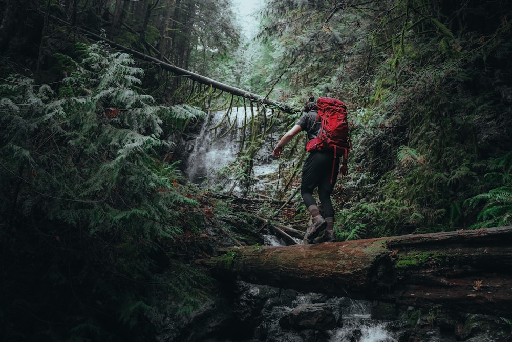 Ein Mann mit rotem Rucksack überquert eine Brücke über einen Bach
