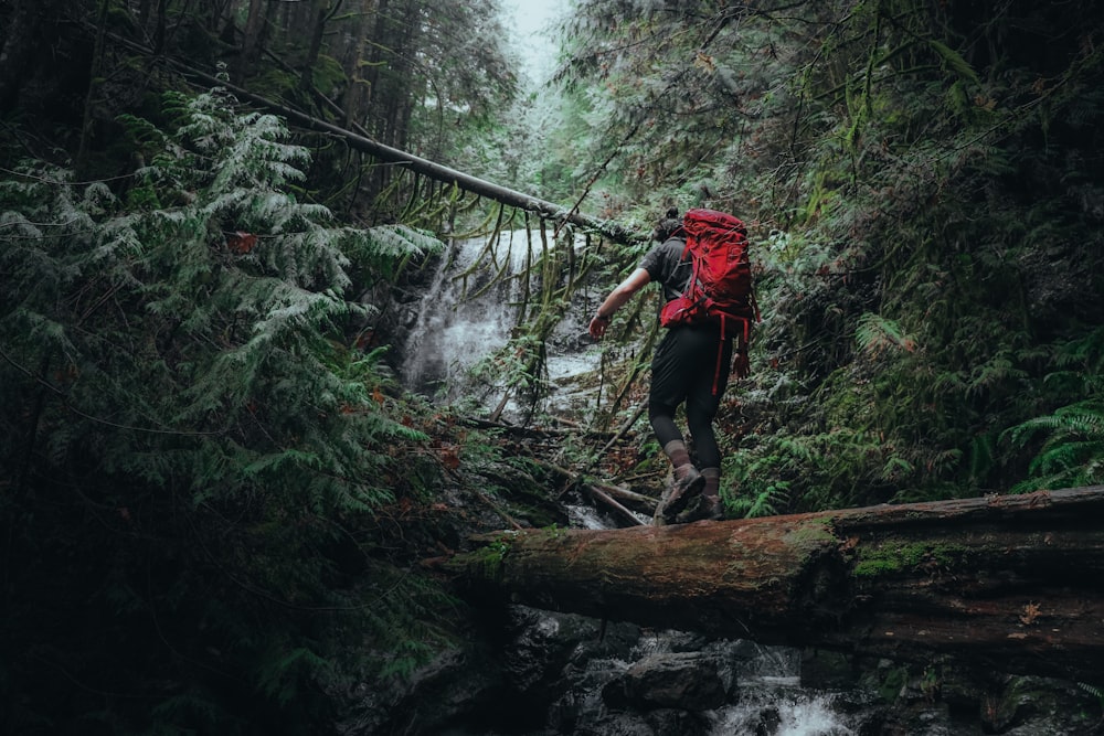 Un hombre con una mochila roja cruza un puente sobre un arroyo