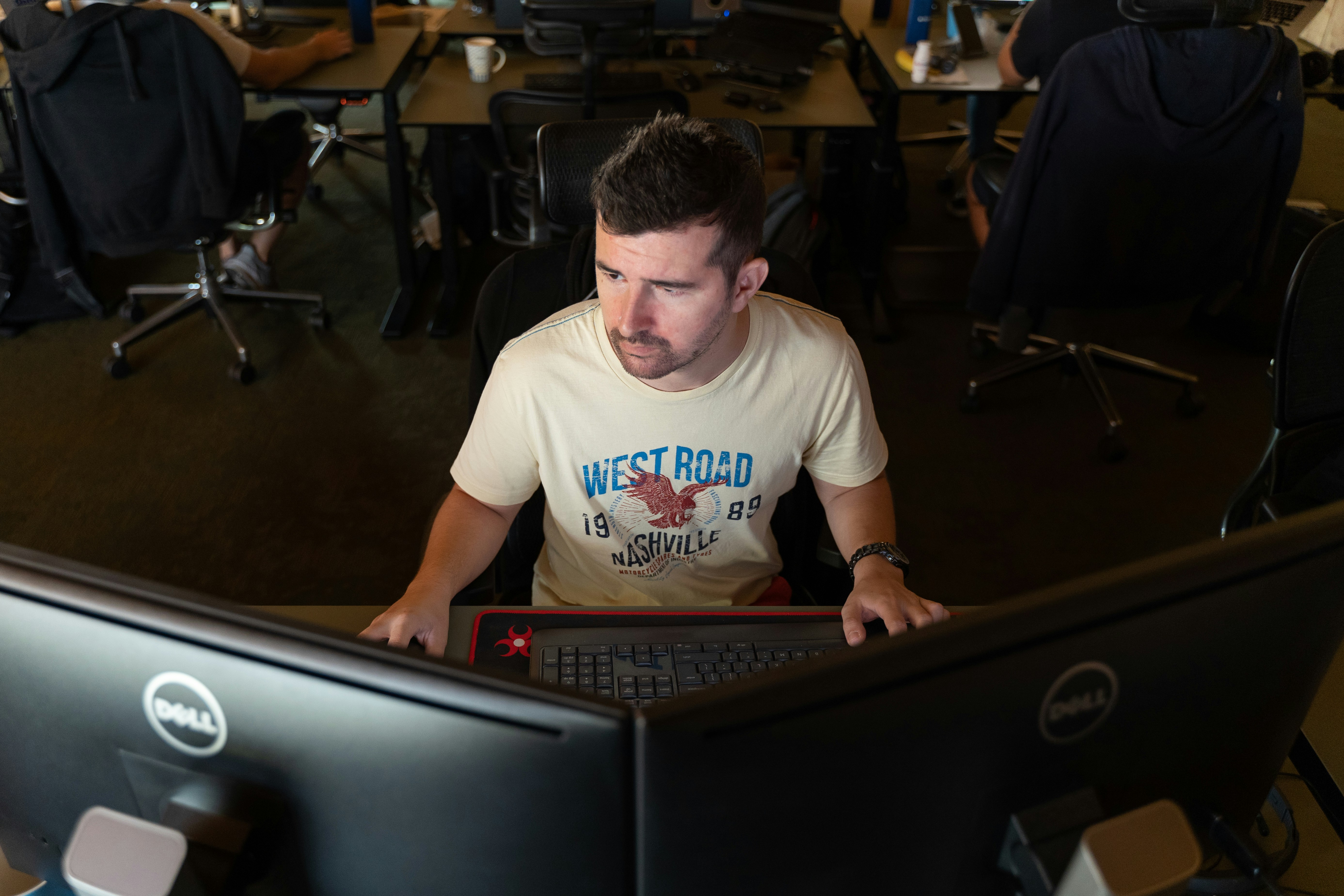 executive typing on laptop keyboard with dual monitors showing productivity software
