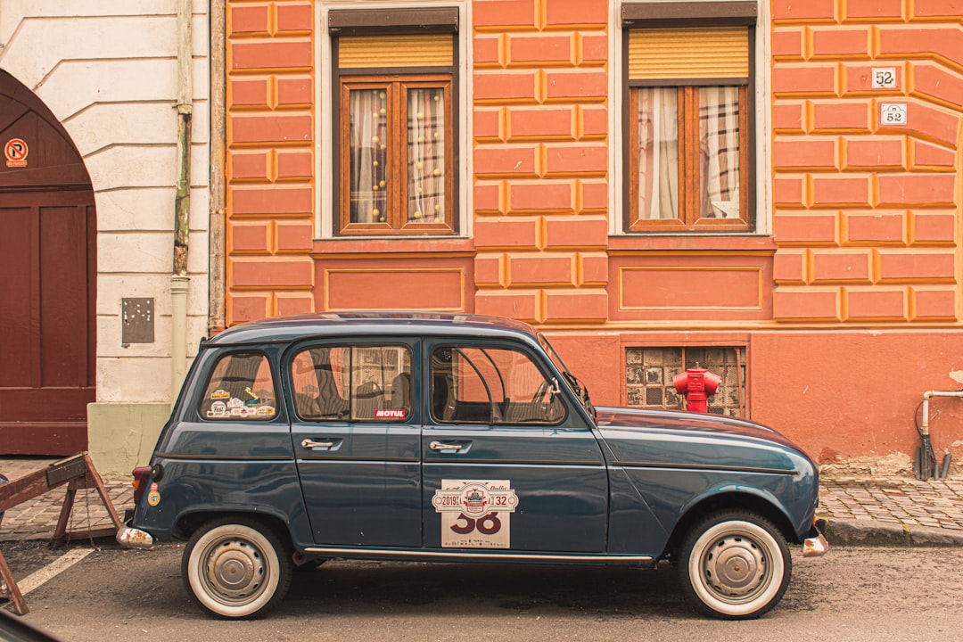 a small blue car parked in front of a building, Old car on a street in Brașov and beautiful buildings