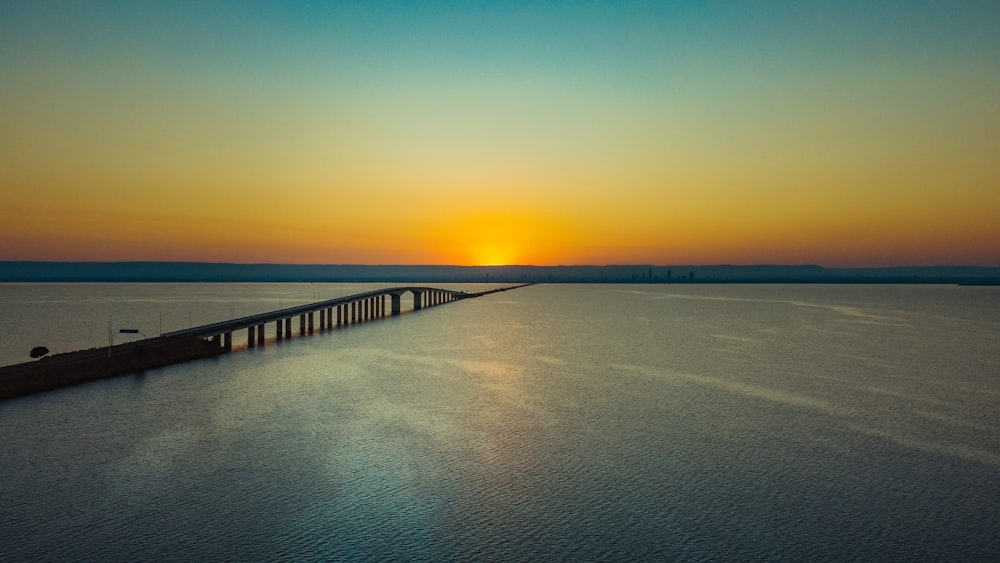 the sun is setting over a long bridge