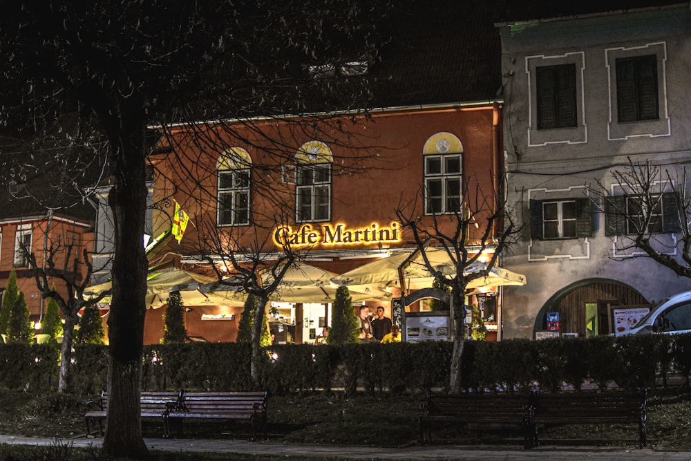 a restaurant lit up at night with a bench in front of it