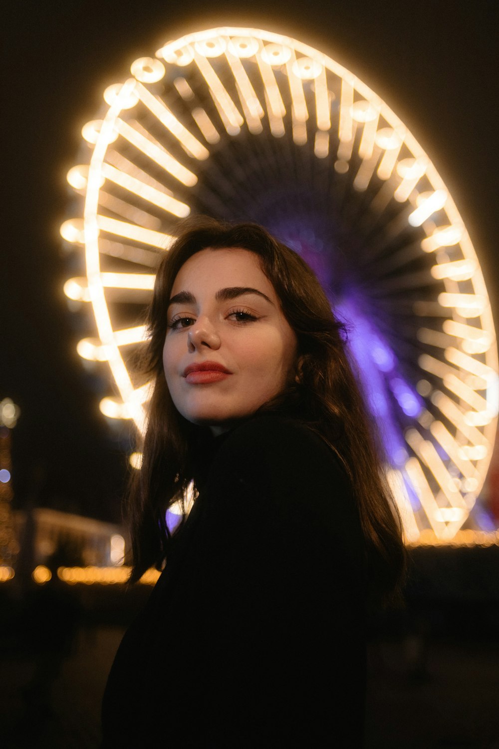 a woman standing in front of a ferris wheel at night