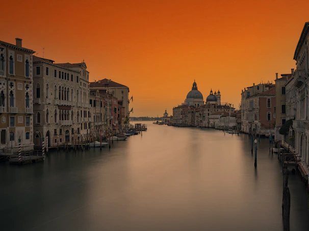 A winding canal in Venice reflecting historic buildings under a soft sunset.