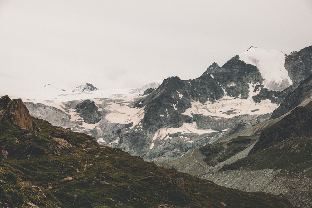 a mountain range covered in snow and green grass