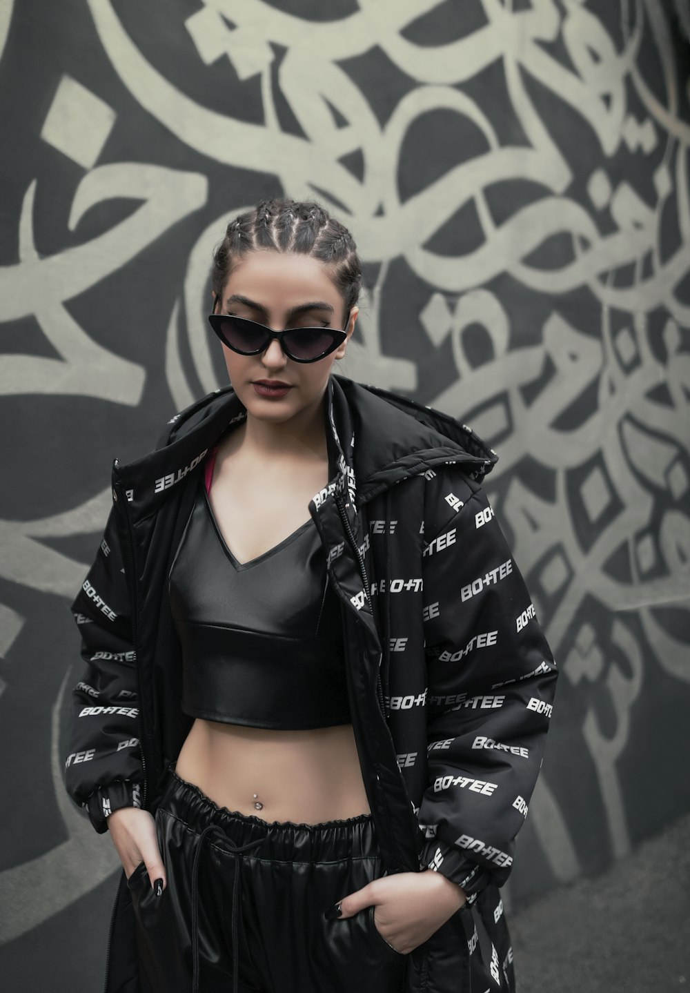 a woman in a crop top and jacket standing in front of a graffiti wall