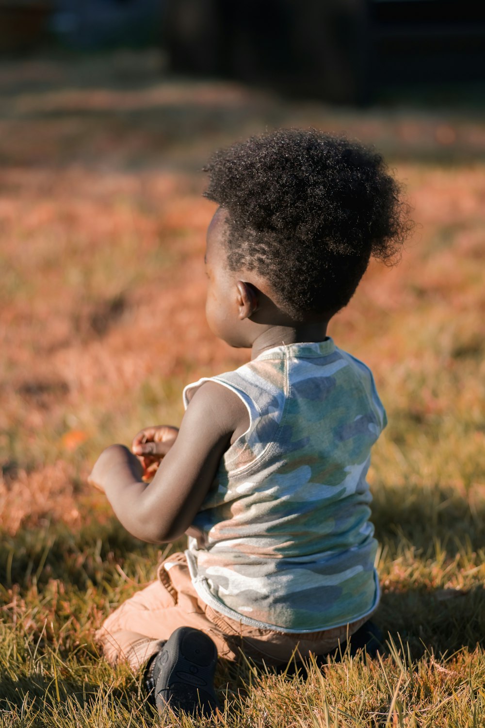 a little boy sitting in the grass holding a piece of fruit