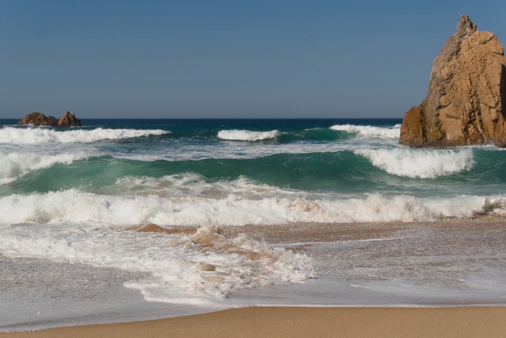 a large rock sticking out of the ocean next to a beach