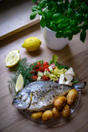 Grilled fresh fish served on a ceramic plate with lemon wedges and herbs.