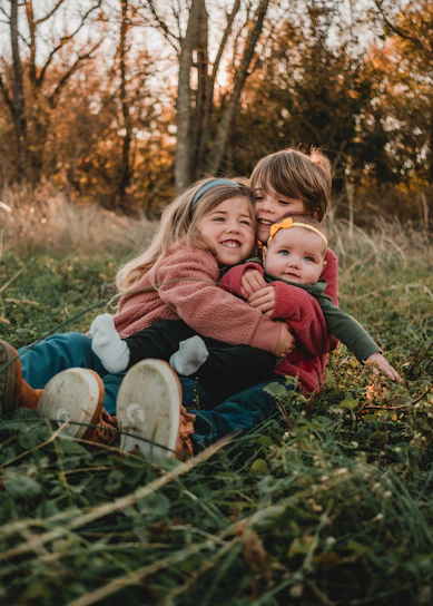 Three children smiling together in a cozy, rustic home setting with their grandmother.