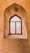 An arched, intricately designed wooden window is set in a brick wall, showcasing ornate geometric patterns. Sunlight filters through, casting detailed shadows on the surrounding bricks. The craftsmanship highlights traditional architectural styles.