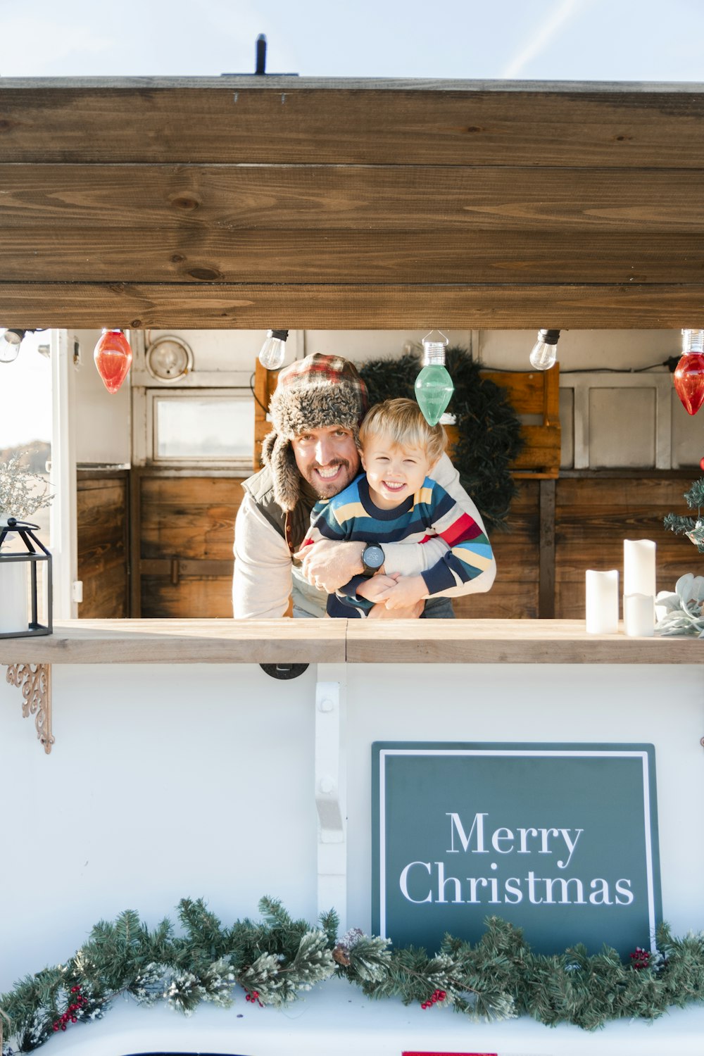 a woman holding a child in front of a merry christmas sign