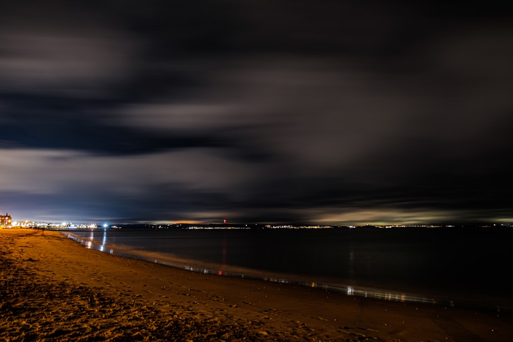a night time view of a beach with a lighthouse in the distance